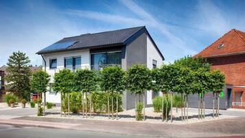 Een modern huis met twee verdiepingen en een plat dak, voorzien van zonnepanelen, gelegen in een verzorgde tuin met jonge bomen en struiken.