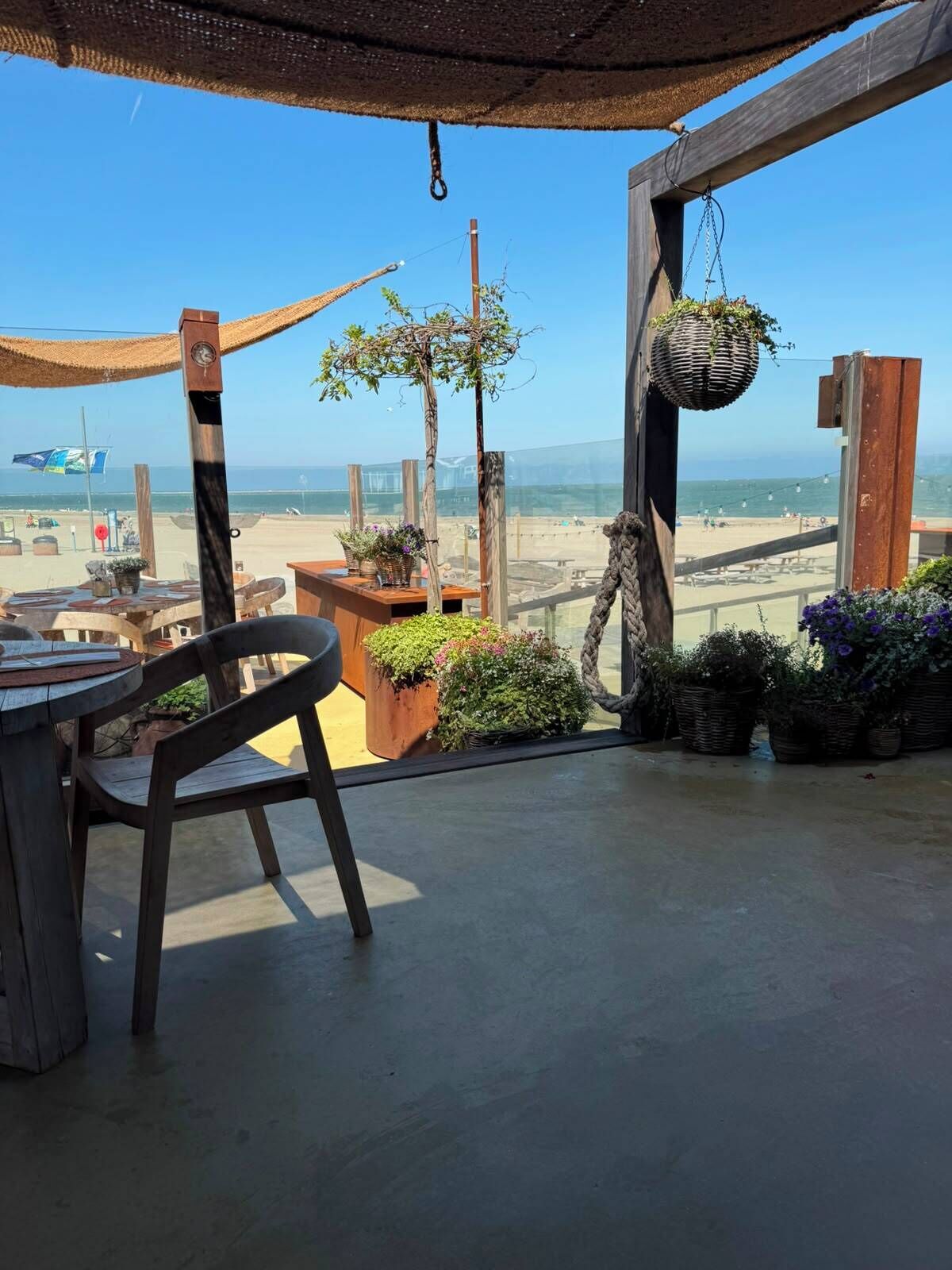 A wooden deck with a table and chairs, overlooking a beach with a clear view of the ocean.