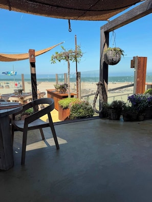 A wooden deck with a table and chairs, overlooking a beach with a clear view of the ocean.