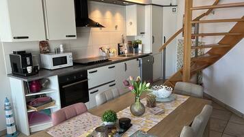 Een moderne keuken met witte kasten, een magnetron, een koffieapparaat en een eethoek met een tafel gedekt voor twee personen.