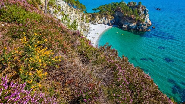 Un paysage côtier avec une plage, des falaises rocheuses et une mer d’un bleu limpide.