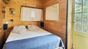 Una habitación de cabaña de madera con una cama, una ventana, un mapa en la pared y un altavoz.