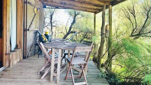 Una terraza de madera con una mesa y sillas, rodeada de árboles y un área techada con techo de madera.