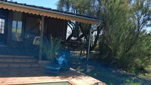 Una piscina con muelle de madera, un porche cubierto con sillas y un edificio con techo inclinado.