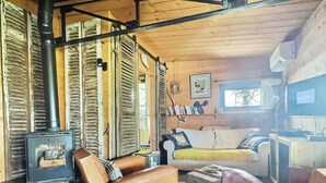 Interior rústico de una cabaña con estufa de leña, sofás de cuero, una estantería y un cuadro enmarcado en la pared.