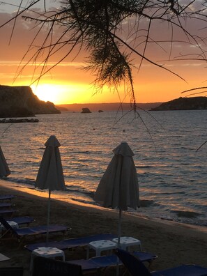 A beach with umbrellas and lounge chairs, a sunset in the background, and calm sea. - Modern villa for 1 to 6 people, private pool, beautiful sea and mountain views (Crete)