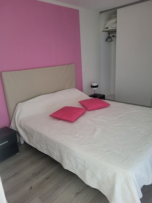 Un dormitorio con cama, mesita de noche, armario y estante colgante.