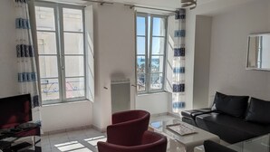 A modern living room with a glass coffee table, red and black sofas, and large windows with patterned curtains.