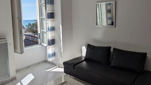A room with a black sofa, a window with patterned curtains, and a mirror on the wall.