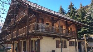 A wooden chalet with a balcony, a covered porch, and a small outdoor seating area. -  Appart 3 ch 6 Pers comfortable 3 * in the cottage Laget (Molines-En-Queyras)