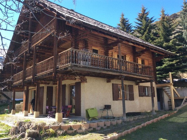A wooden chalet with a balcony, a covered porch, and a small outdoor seating area.