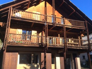 A two-story wooden cabin with a balcony, large windows, and a wooden deck.