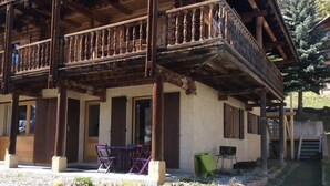 A wooden building with a balcony, a table with chairs, and a small garden area. -  Appart 3 ch 6 Pers comfortable 3 * in the cottage Laget (Molines-En-Queyras)