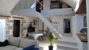 A spacious loft-style living area with a high ceiling, a staircase leading to an upper level, a dining area, and a stone wall.