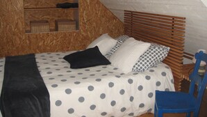 A bedroom with a sloped ceiling, wooden headboard, and a bed with polka dot bedding.