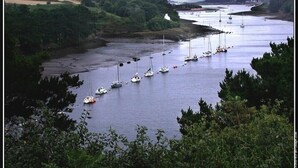 A coastal landscape with a river, boats, and greenery.