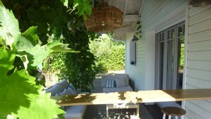 Un espace extérieur abrité, aménagé avec une table et des tabourets en bois, un banc rembourré et un luminaire suspendu.