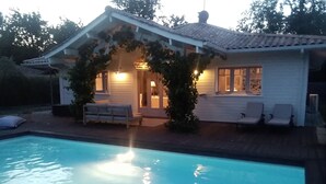 Une maison avec une piscine, un patio couvert avec des sièges et un intérieur bien éclairé.