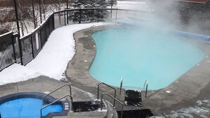 Ein Poolbereich mit Whirlpool und kleinem Schwimmbecken, umgeben von einem mit Schnee bedeckten Deck und einem Metallzaun.