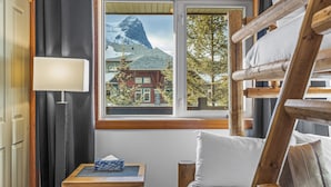 Ein Zimmer mit einem Etagenbett, einem Nachttisch mit Taschentuchbox, einem Fenster mit Blick auf einen Berg und Gebäude sowie einer Wandlampe.