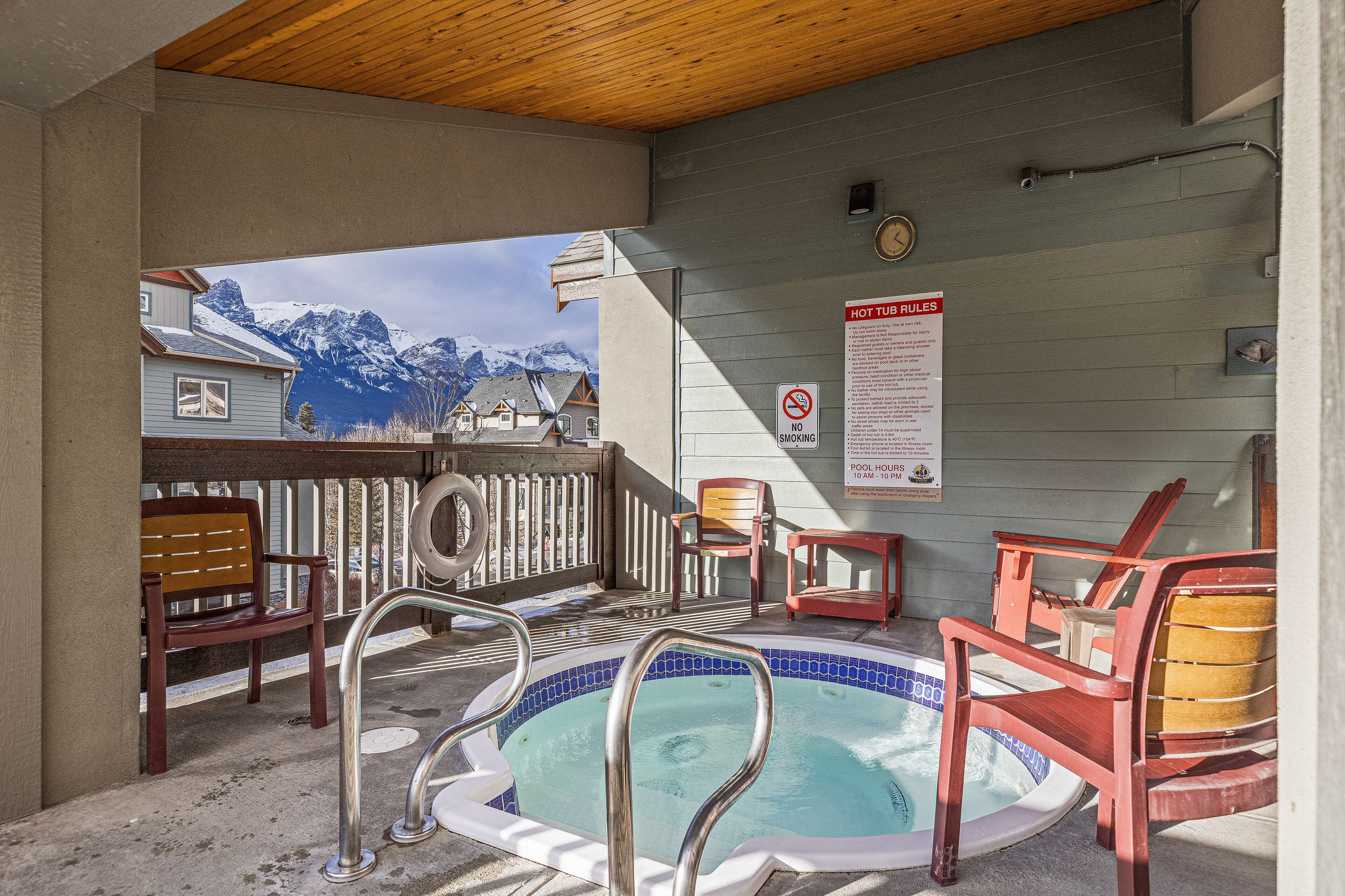 A pool area with a hot tub, chairs, and a view of snow-capped mountains.