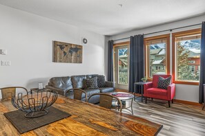 A modern living room with a wooden dining table, leather sofa, and a red armchair.