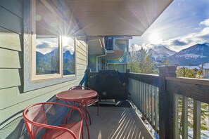 A balcony with a grill, two red chairs, and a view of mountains. - Cozy Canmore Condo for 7🍁Modern Rustic Mountain Escape⛰☀️Outdoor Pool & Hot Tubs☀️ (Canmore)