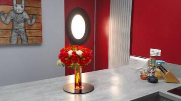 Une cuisine moderne avec un plan de travail en marbre, un vase rempli de fleurs rouges et un four fixé au mur.