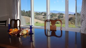 Une table à manger donnant sur un paysage grâce à de grandes fenêtres.