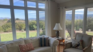 Un salon comprenant un canapé, un fauteuil et une table basse, de grandes fenêtres offrant une vue sur les montagnes et la verdure.