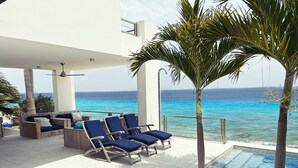 A poolside area with lounge chairs and a palm tree, overlooking a clear blue ocean. - ❤ Exceptional oceanfront vacation ✔ (Kralendijk (Punt Vierkant))