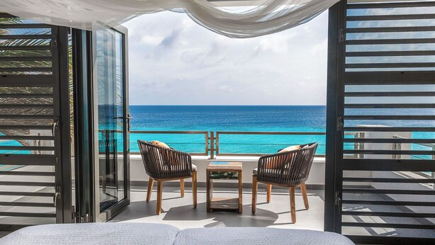 A balcony with a view of the ocean, two wicker chairs, a small table, and a bed. - ❤ Exceptional oceanfront vacation ✔ (Kralendijk (Punt Vierkant))