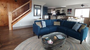 Un salon spacieux avec un canapé d’angle bleu, une table basse en verre et un escalier en bois.