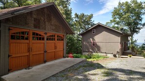 Un bâtiment à deux étages, doté d’un garage et d’un petit abri de jardin, entouré d’arbres et bordé d’une allée en gravier.