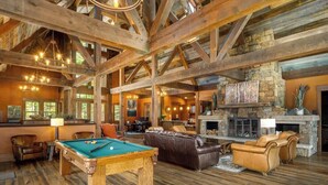 Una habitación amplia con mesa de billar, sofás de cuero y chimenea de piedra.