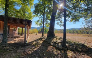 A rustic cabin with a wooden deck, surrounded by large trees and a stone pathway.