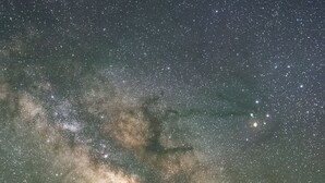 Un granero de madera rústico bajo un cielo estrellado donde se distingue la Vía Láctea.