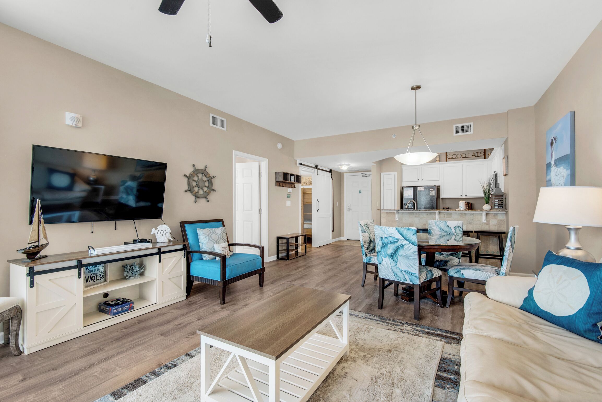 A spacious living room with a TV, seating, a dining area, and a kitchen in the background.