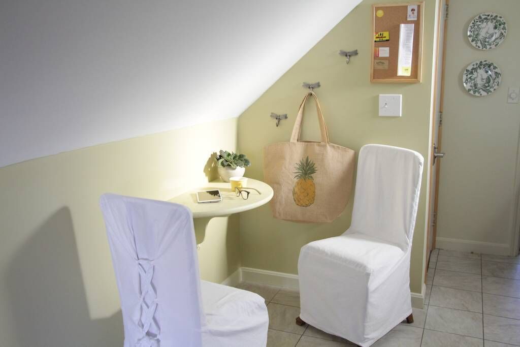 A room with a white chair, a white table with a plant, a wall-mounted bulletin board, and a door with a plate decoration.