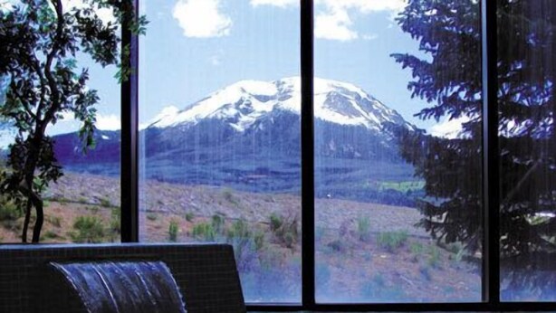 Un jacuzzi con vistas a una montaña nevada a través de amplios ventanales.