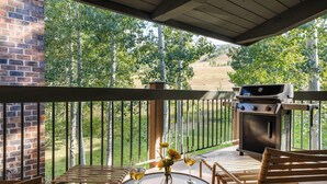 A covered patio with a brick wall, a grill, and a table with chairs and wine glasses. - Top of the Village~Ski-in/out~HT~Pool~Grill~Parking (Snowmass Village)