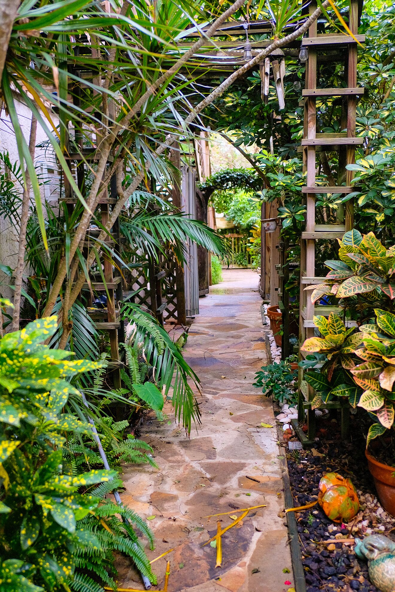 A stone pathway flanked by lush greenery and wooden structures in a garden setting.
