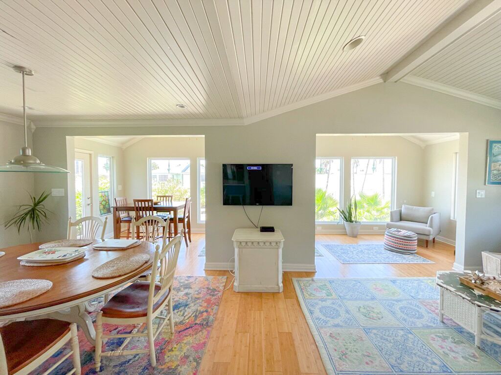 A spacious living room with a wooden dining table, a flat-screen TV mounted on the wall, and a cozy seating area with a sofa and armchairs.