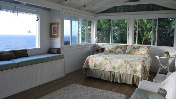 Una camera da letto con vista sull'oceano, un letto con biancheria da letto floreale, una panca finestrella e un tavolino con una lampada.