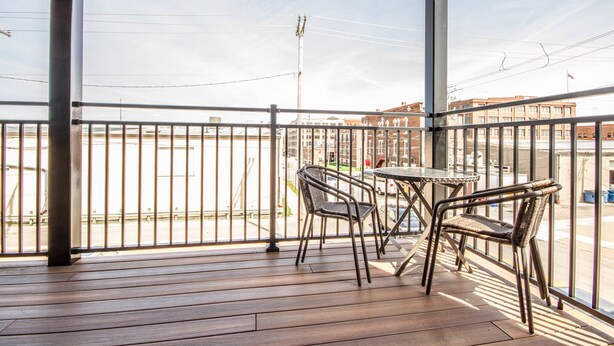 Een balkon met een houten vloer, een metalen hekwerk en twee rieten stoelen.