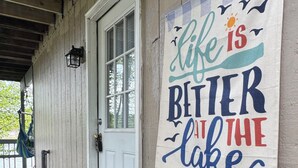 Un portico in legno con una porta bianca, un tappetino d'ingresso e un cartello con una frase motivazionale al muro.