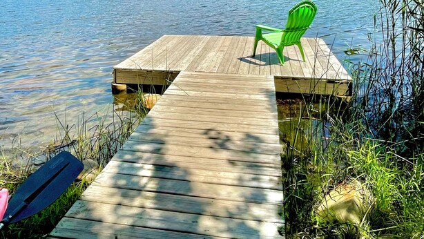 Un molo di legno che si protende in un lago, con una sedia verde sopra.