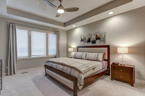 Ein Schlafzimmer mit Bett, Nachttischen, einem Deckenventilator und einem Fenster mit Jalousien.