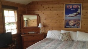 A wooden cabin room with a bed, dresser, television, and a poster of New York.