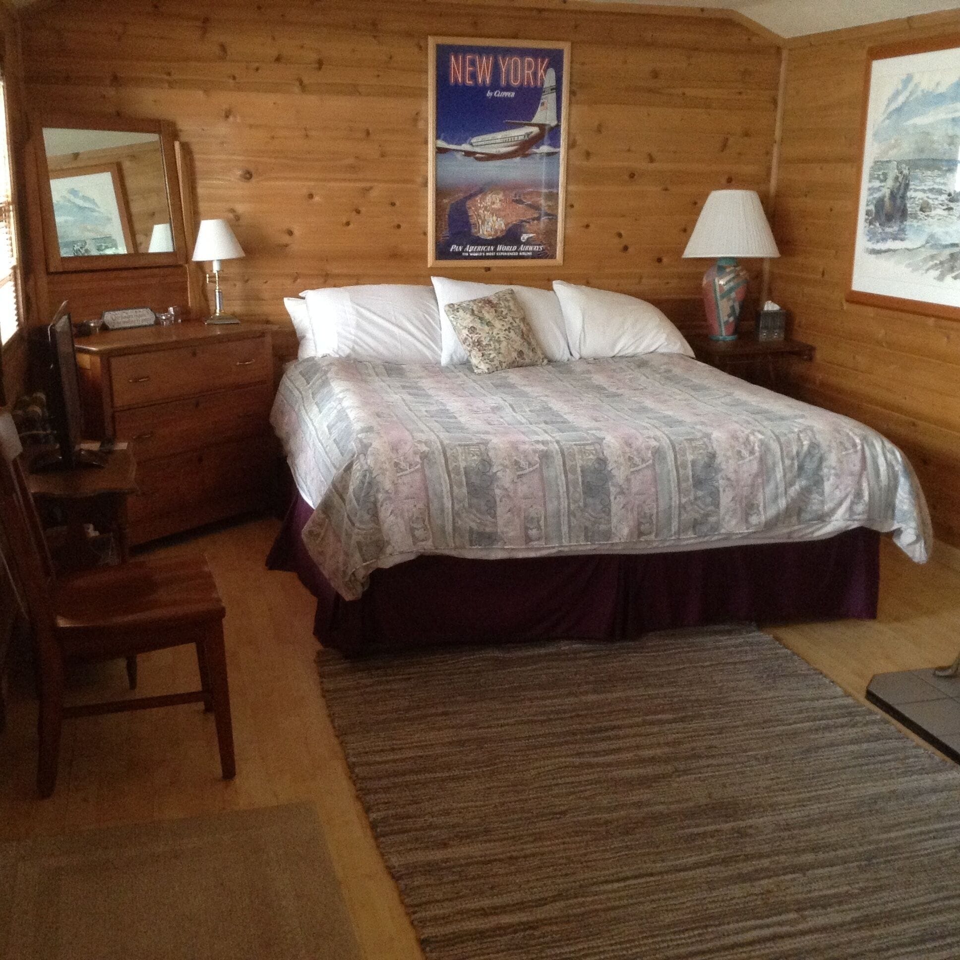 A wooden cabin-style bedroom with a bed, dresser, and a poster of a ship on the wall.